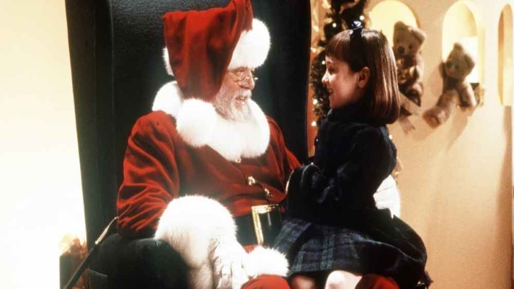 Een meisje dat bij de kerstman op schoot zit.