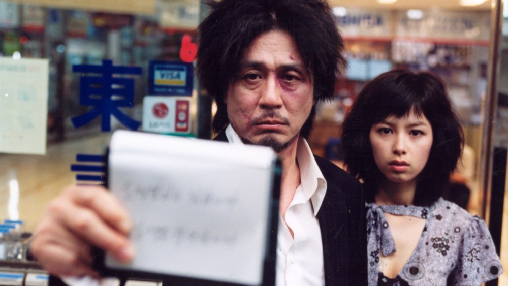 A man with a bruised face holding up a notepad at a store, standing beside a younger woman.