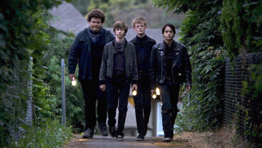 A group of 4 young teenagers walking side by side and holding flashlights.