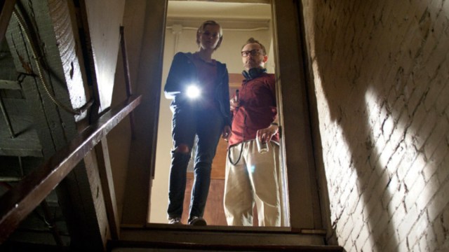 A woman and man holding a flashlight and looking down a flight of stairs.