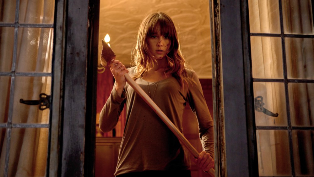 A woman holding an axe, standing in front of a window.