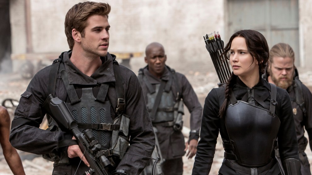 Katniss Everdeen (Jennifer Lawrence) and Gale Hawthorne (Liam Hemsworth) in military gear walking through rubble.