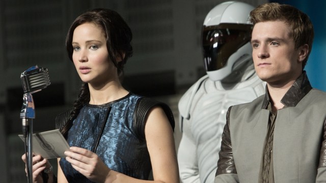 Katniss Everdeen (Jennifer Lawrence) and Peeta Mellark (Josh Hutcherson) presenting a speech in front of an armed guard in 'The Hunger Games: Catching Fire'.