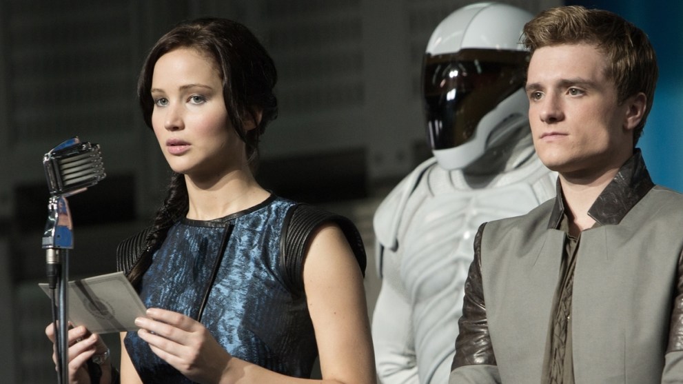 Katniss Everdeen (Jennifer Lawrence) and Peeta Mellark (Josh Hutcherson) presenting a speech in front of an armed guard in 'The Hunger Games: Catching Fire'.