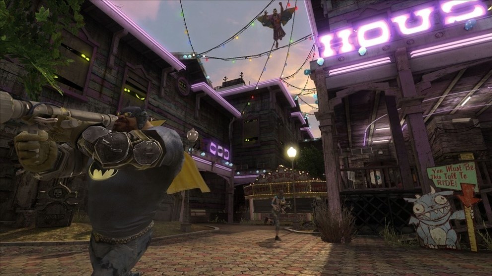 A large, brutish man is seen in the foreground holding a rocket launcher and wearing a Batman costume.  The location is a neon-trimmed carnival-esque town.