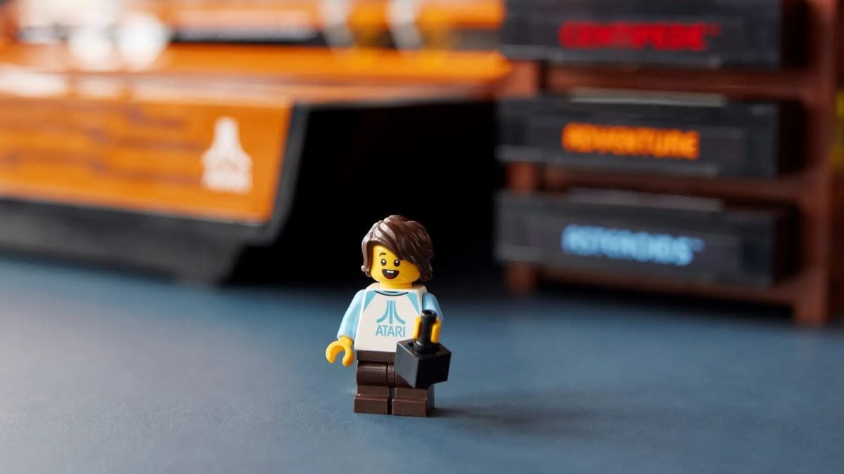 A LEGO Minifigure with an Atari t-shirt stands in front of a LEGO construction of the Atari 2600 game system