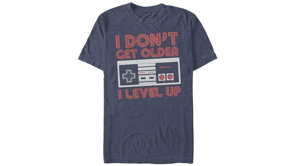 NES 컨트롤러가 달린 회색 파란색 닌텐도 셔츠, 그리고 '나이가 들지 않아 레벨업한다'는 문구가 빨간색 글씨로 적혀 있음
